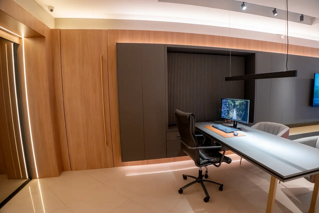Home office planejado com painel ripado, bancada de trabalho ampla e iluminação suspensa.