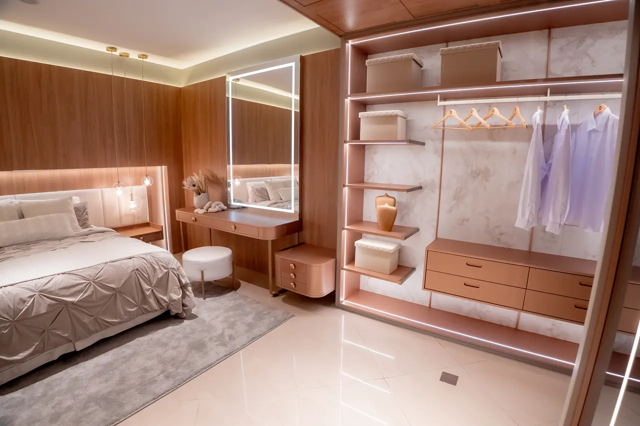 Closet planejado aberto com cabideiros iluminados, gaveteiros em madeira e prateleiras sob medida.