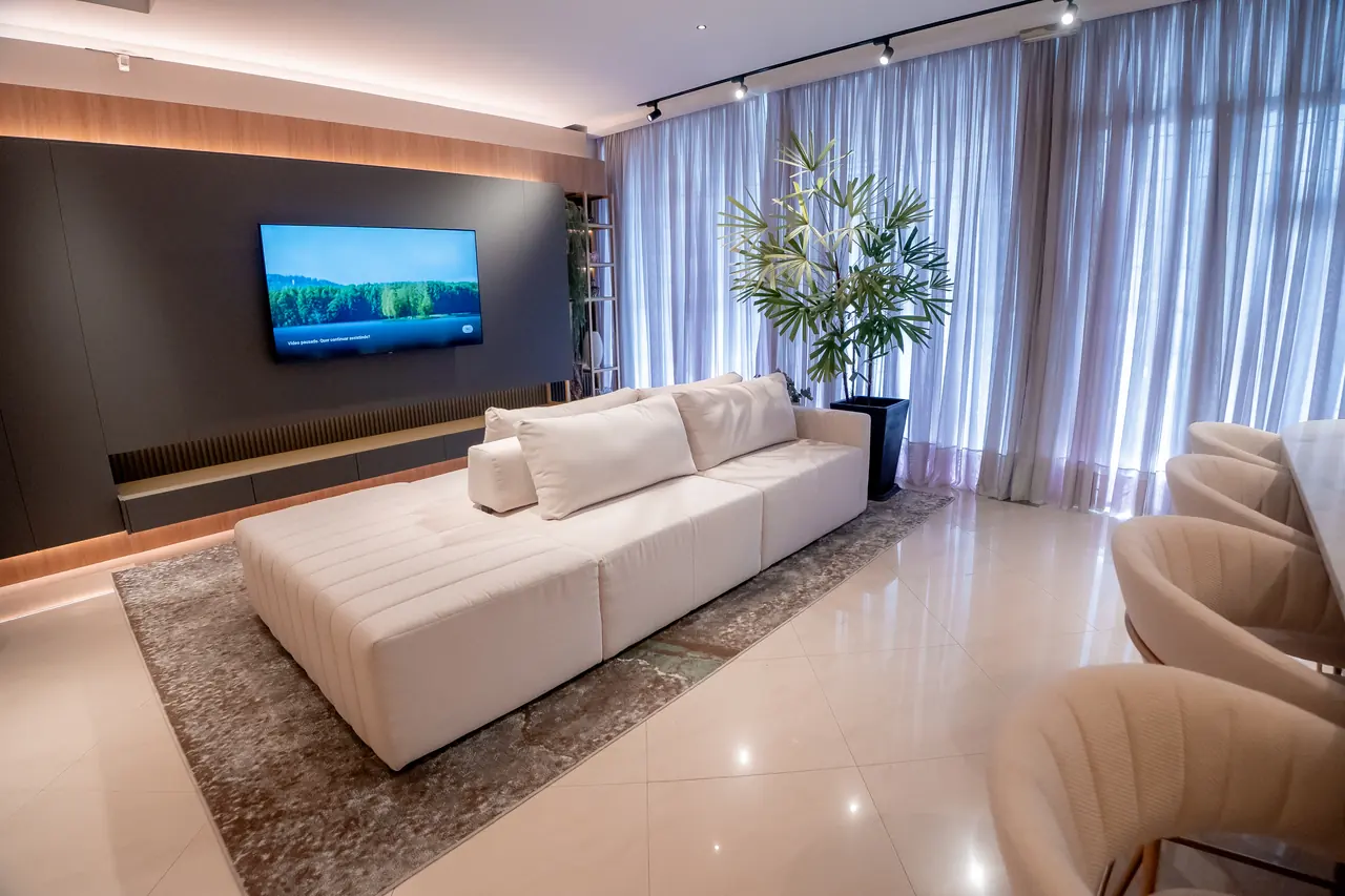 Sala de estar planejada com painel de TV em tom grafite, sofá amplo e iluminação linear no forro.