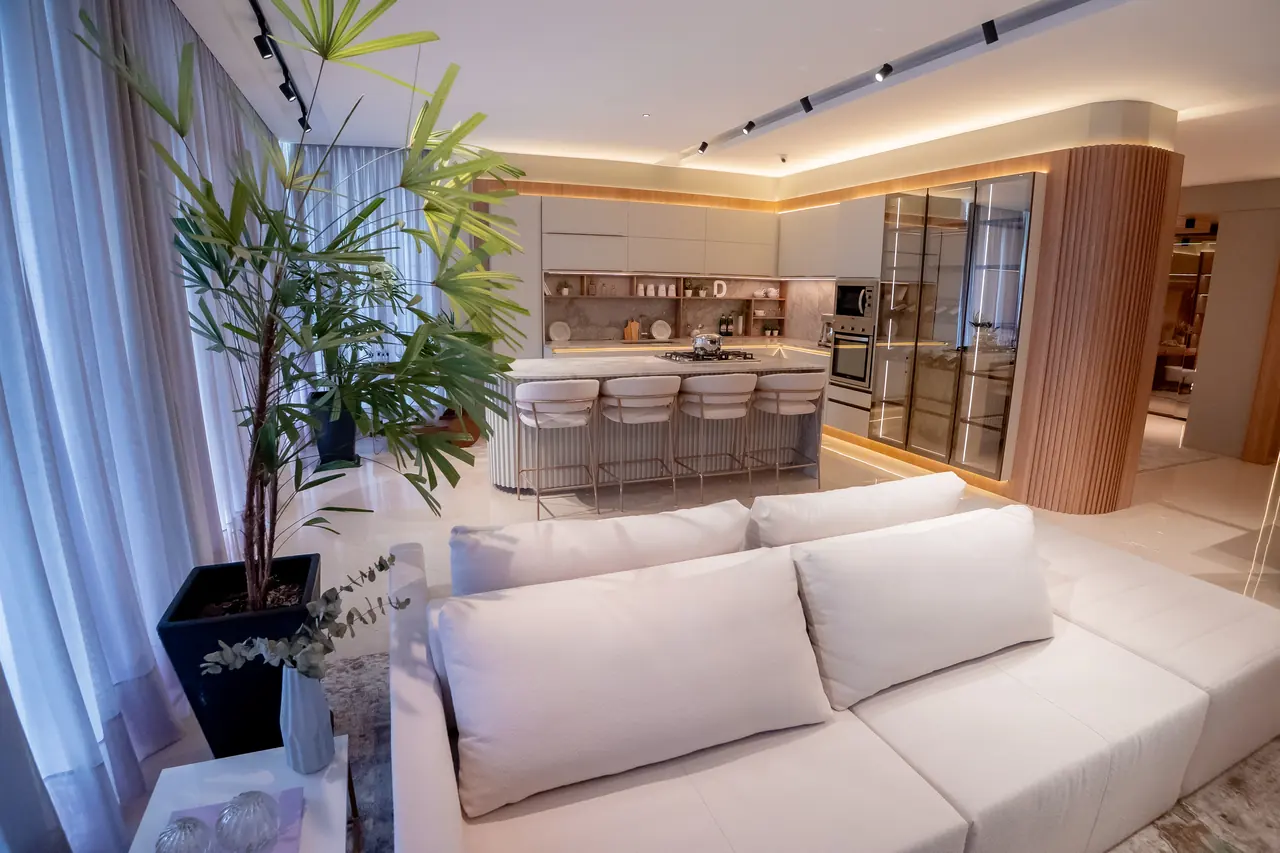 Sala integrada à cozinha por marcenaria ripada curva, com sofá claro e paisagismo interno.